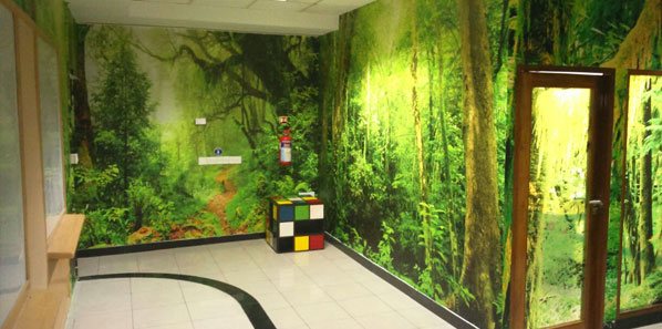 Green forest mural wrapping an EdgeVerve breakout corridor with a colour cube seat.
